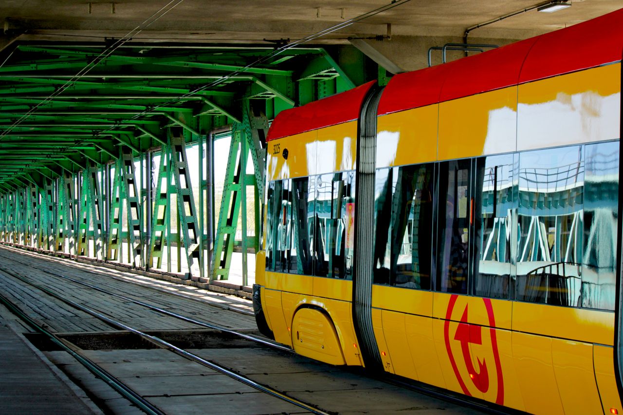 mission-img Modern yellow tram traversing an urban green steel bridge, showcasing urban transit infrastructure.