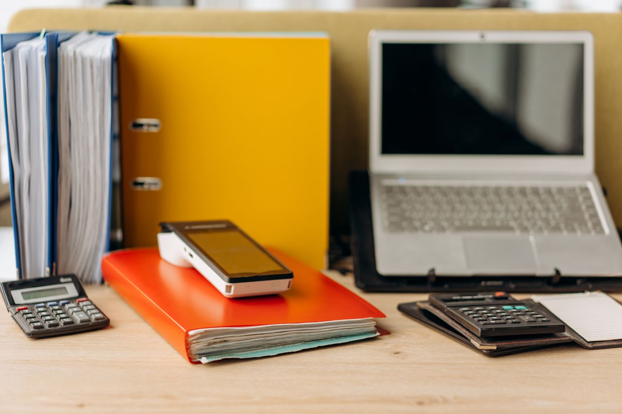 Office desk setup with laptop, documents, and calculators, ideal for business productivity.